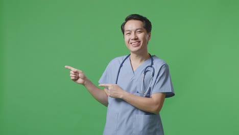 médico masculino asiático con estetoscopio sonriendo y señalando al lado en el fondo de la pantalla verde en el hospital