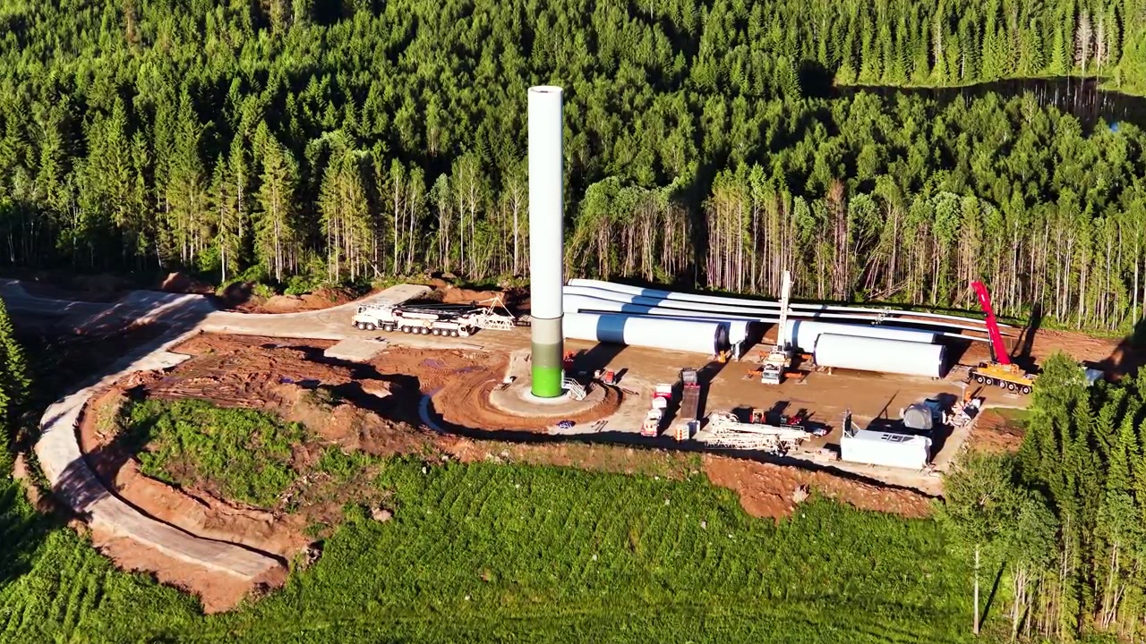 Aerial view of wind turbine construction site with tower and blades in forest