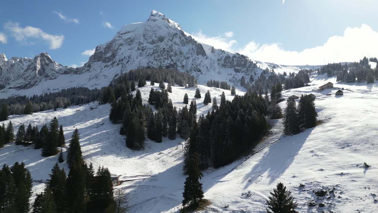 Aerial drone shot flying over snow covered mountain slope along the rural area of Fronalpstock, Switzerland Glarus on a cold winter day