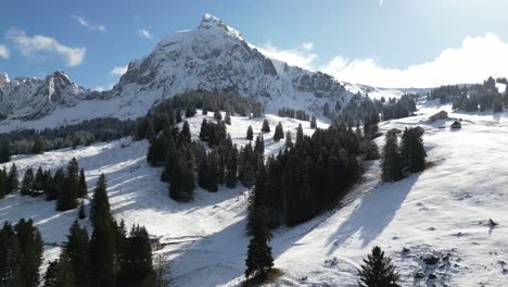 Aerial-drone-shot-flying-over-snow-covered-mountain-slope-along-the-rural-area-of-Fronalpstock,-Switzerland-Glarus-on-a-cold-winter-day