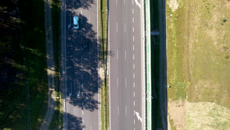 Von-Oben-Nach-Unten-Aufgenommene-Luftaufnahme-Einer-Autobahn-Mit-Fahrzeugen,-Flankiert-Von-Grün-Und-Schatten