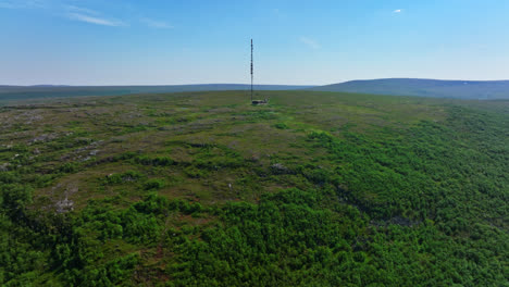 Drone-rising-over-a-fell-toward-a-radio-tower-on-top,-summer-in-Utsjoki,-Finland