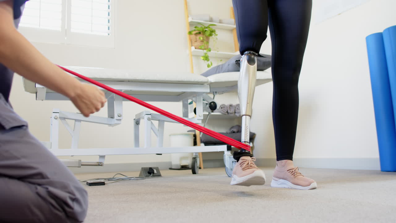 A person with prosthetic leg standing while another adjusting resistance band