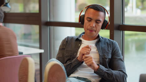 Young-Businessman-With-Feet-On-Desk-In-Office-Listens-To-Music-On-Wireless-Headphones-Air-Drumming