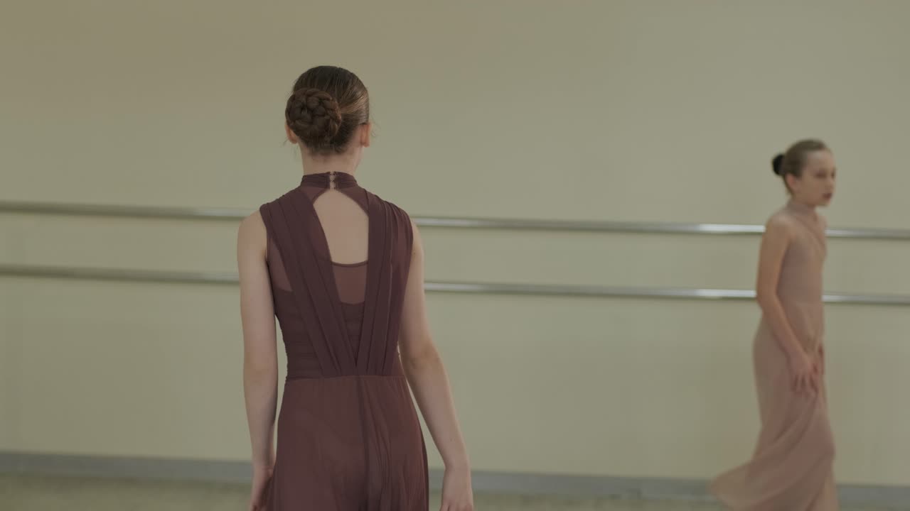 Un grupo de jóvenes estudiantes de ballet con ropa de baile negra practicando posiciones en un espacioso estudio de ballet con suelo de madera y barras de pared. Expresiones de concentración y movimientos sincronizados