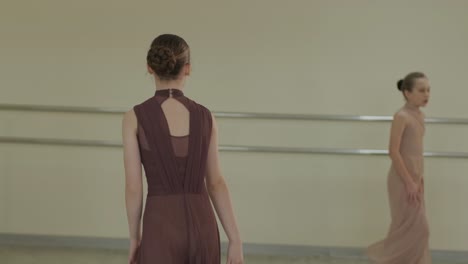 a group of young ballet students in black dancewear practicing positions in a spacious ballet studio with wooden flooring and wall-mounted barres. focused expressions and synchronized movements.