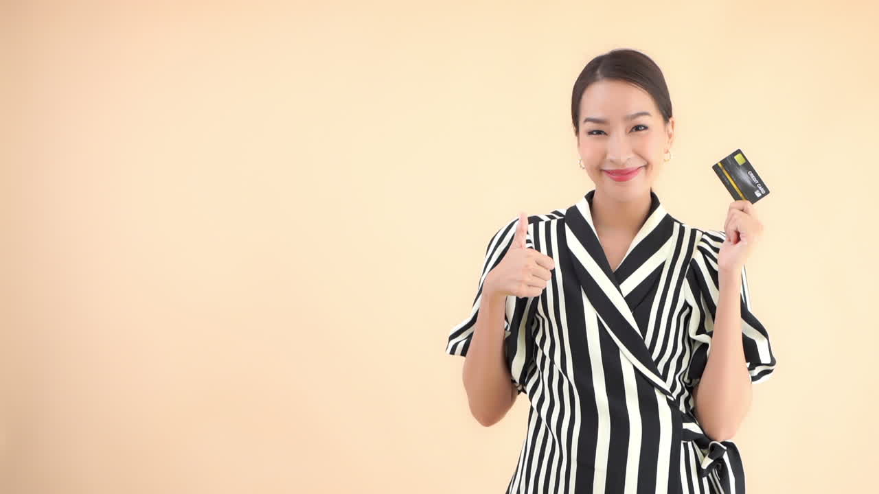 Young lady holding a credit card or a debit card in her handand showing ok gesture on isolated background