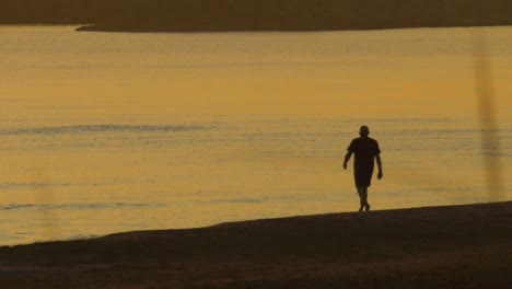 Silhouette-Eines-Mannes-Mittleren-Alters,-Der-Im-Morgengrauen-An-Der-Friedlichen-Küste-Spazieren-Geht,-Zeitlupe