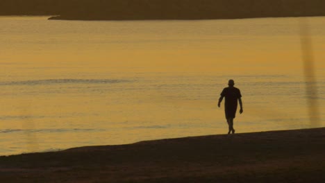 silueta de un hombre de mediana edad caminando por la tranquila orilla del mar al amanecer, a cámara lenta