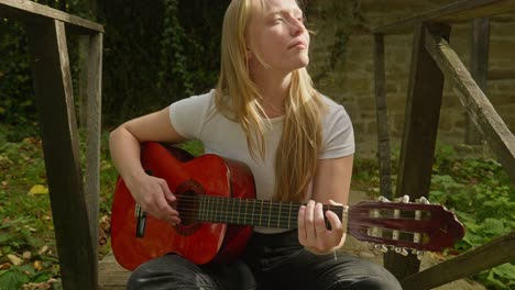 una joven rubia hermosa toca la guitarra acústica un puente de madera rústico