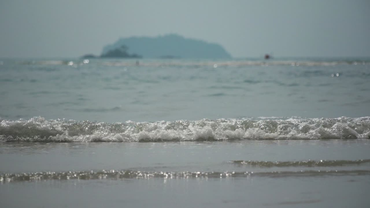 슬로우 모션, 작은 파도가 멀리 흐릿한 산과 함께 굴러 들어옵니다.