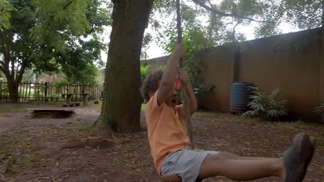 slow motion shot of a young boy holding onto a rope swing attached to a tree in a backyard