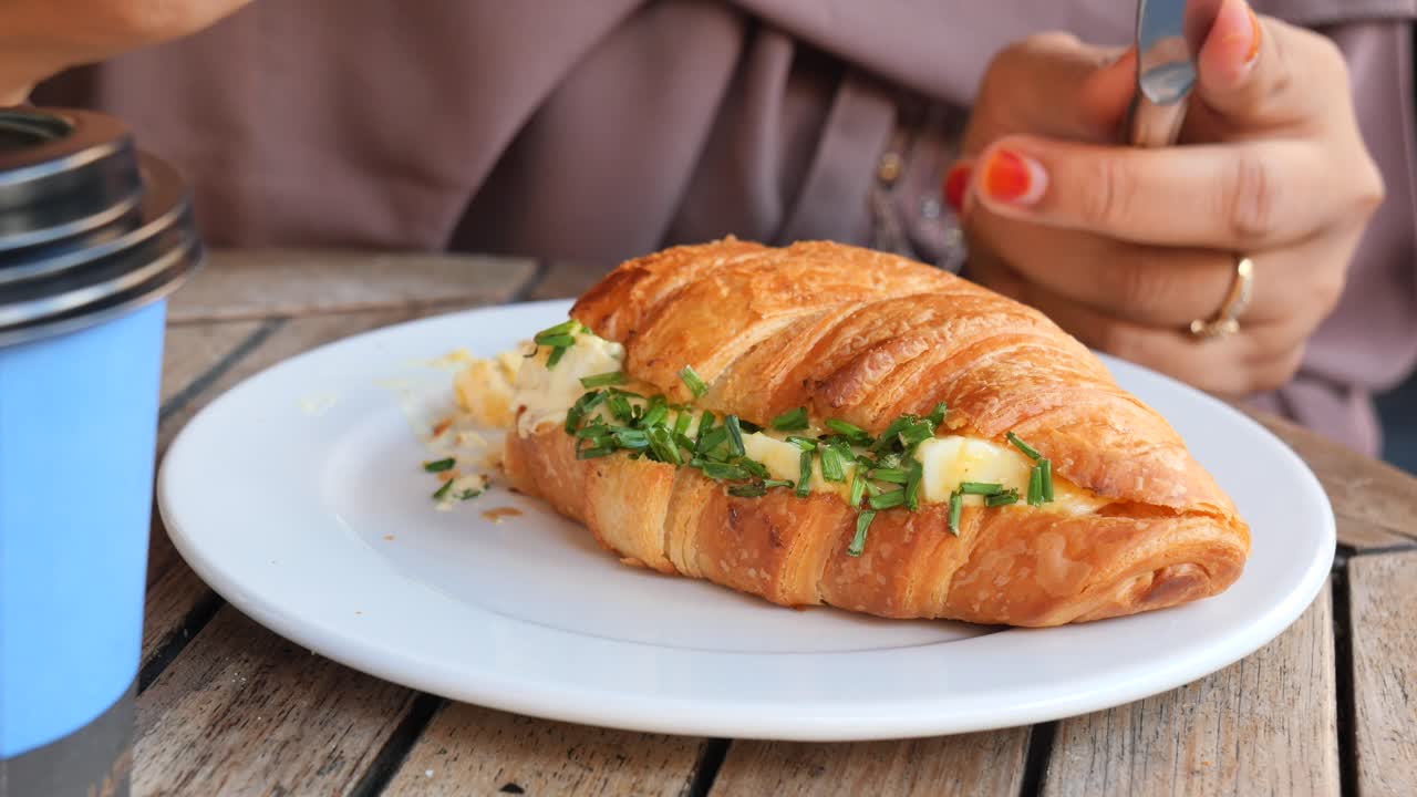 Kvinne spiser en croissant-sandwich
