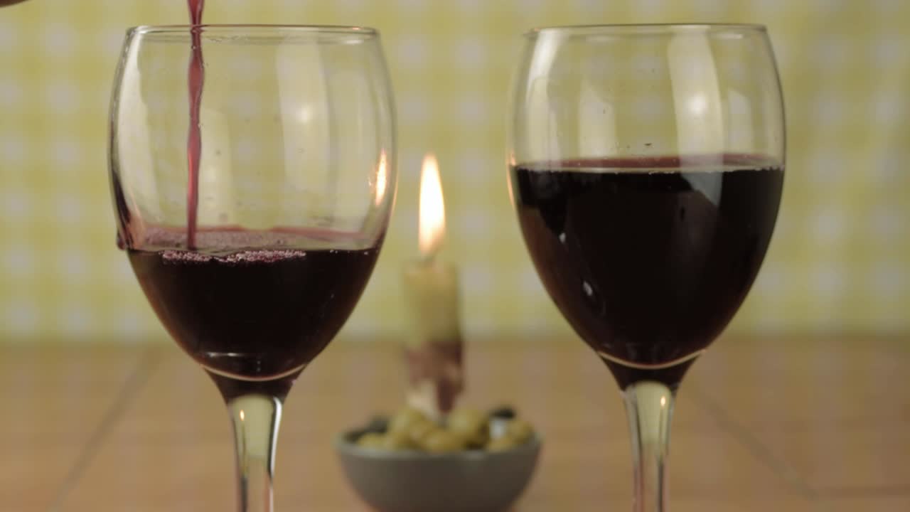 Versando vino rosso in un bicchiere con una candela, inquadratura media.