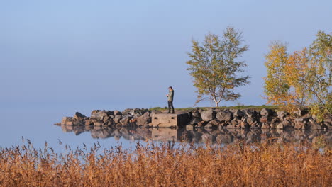 Alone-man-standing-on-small-headland-on-peaceful-autumn-day,-sky-and-water-intertwined