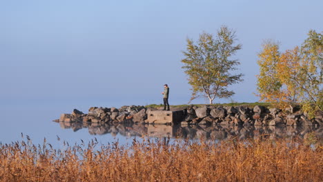 alone man standing on small headland on peaceful autumn day, sky and water intertwined