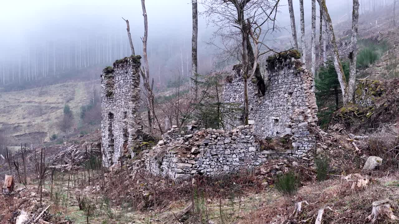 aérea ampliada en órbita alrededor de ruinas de granjas muy antiguas en una montaña con bosque y niebla