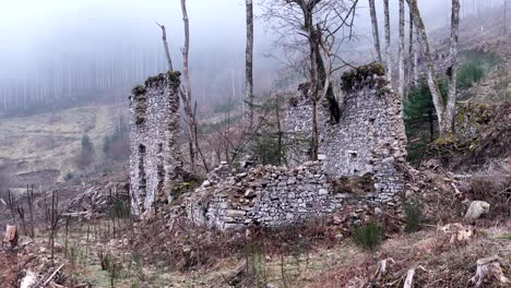 Aerial-zoomed-in-orbit-around-very-old-farm-ruins-on-a-mountain-with-forest-and-fog