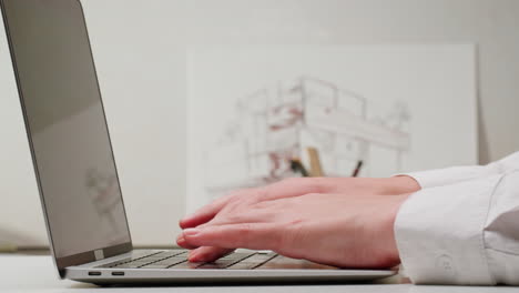 person typing on a laptop with architectural design sketch in background