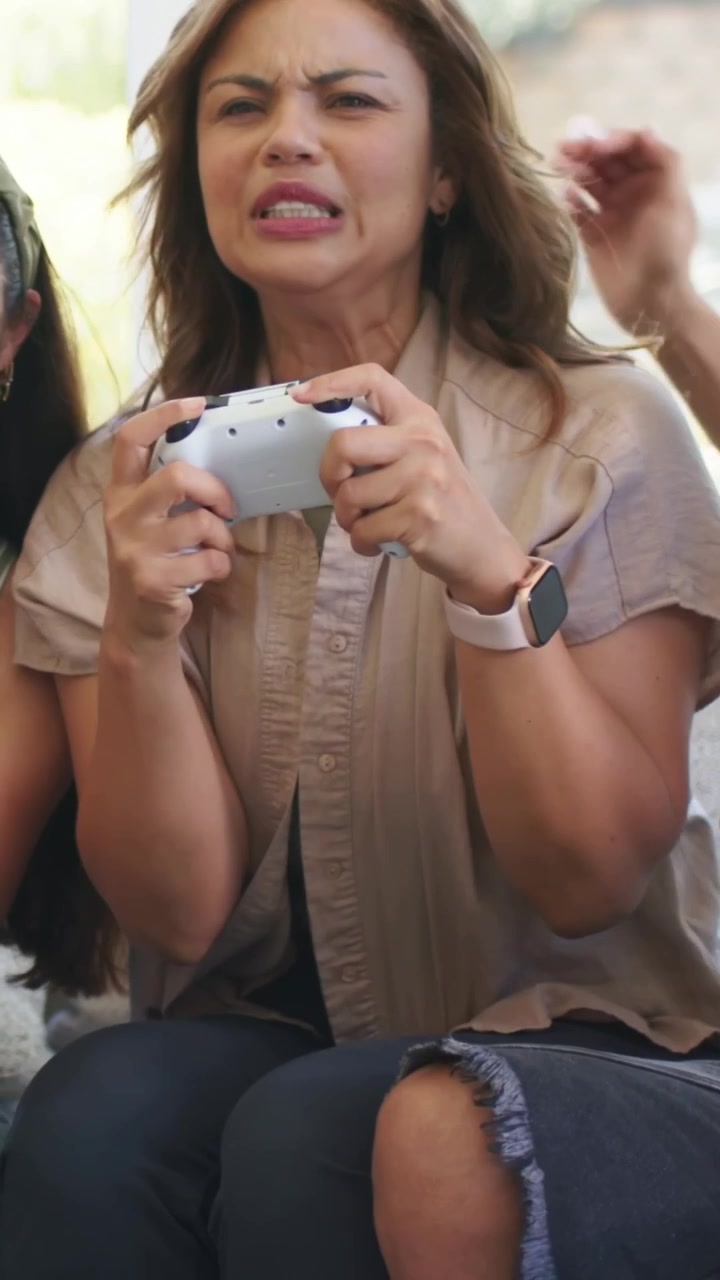 Vertical video: Laughing man in gray T at home holding green bottle seeing and reaching for gamepad