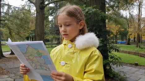 young girl with yellow raincoat studying a map in park