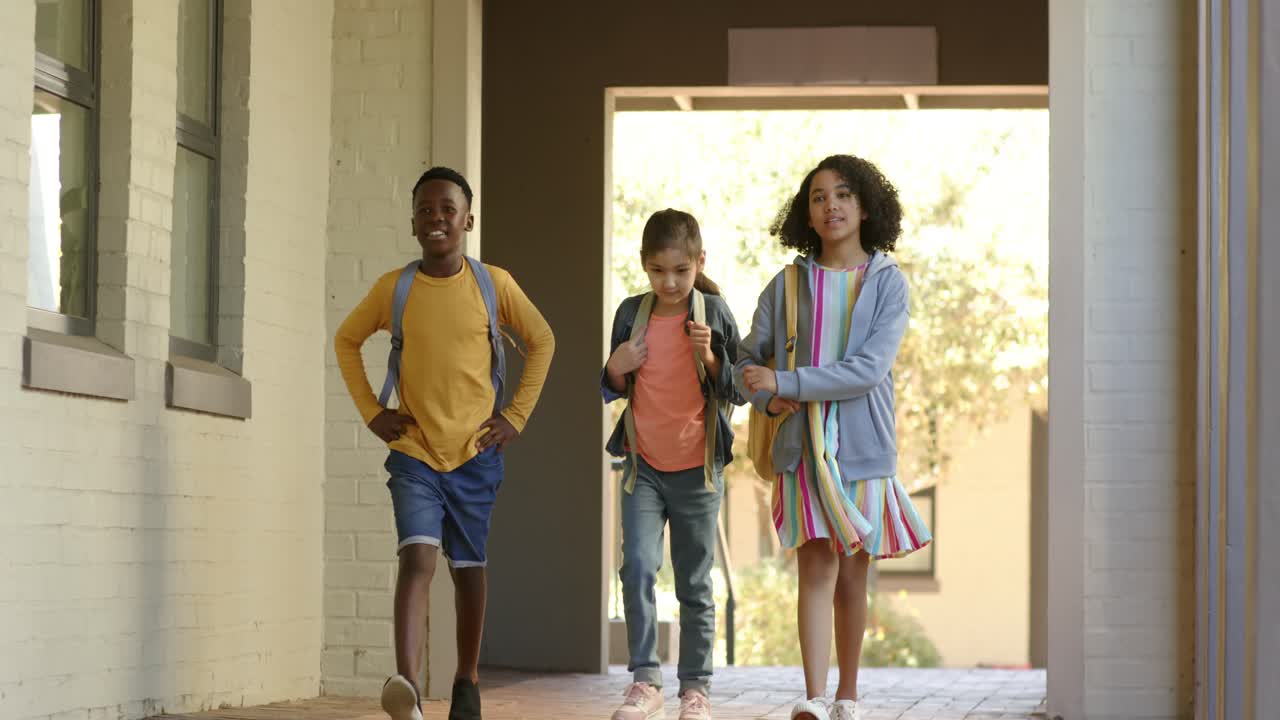 Diverse child friends walking from sunlit yard into corridor, adjusting backpacks, heading to class