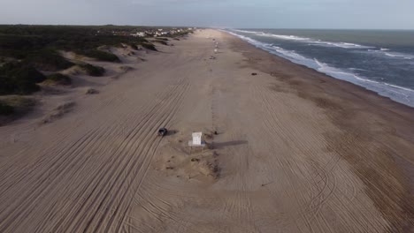 Siguiente-Toma-Aérea-Del-Camión-De-Cuatro-Ruedas-Que-Sale-De-La-Playa-Y-Conduce-Por-Un-Camino-Forestal-Rural-Junto-A-Las-Olas-De-Agua-De-La-Playa-En-América-Del-Sur,-Argentina