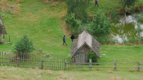 Pareja-Caminando-Por-Una-Cabaña-De-Madera-En-El-Exuberante-Paisaje-En-Piaszno,-Voivodato-De-Pomerania,-Polonia---Tiro-De-ángulo-Alto