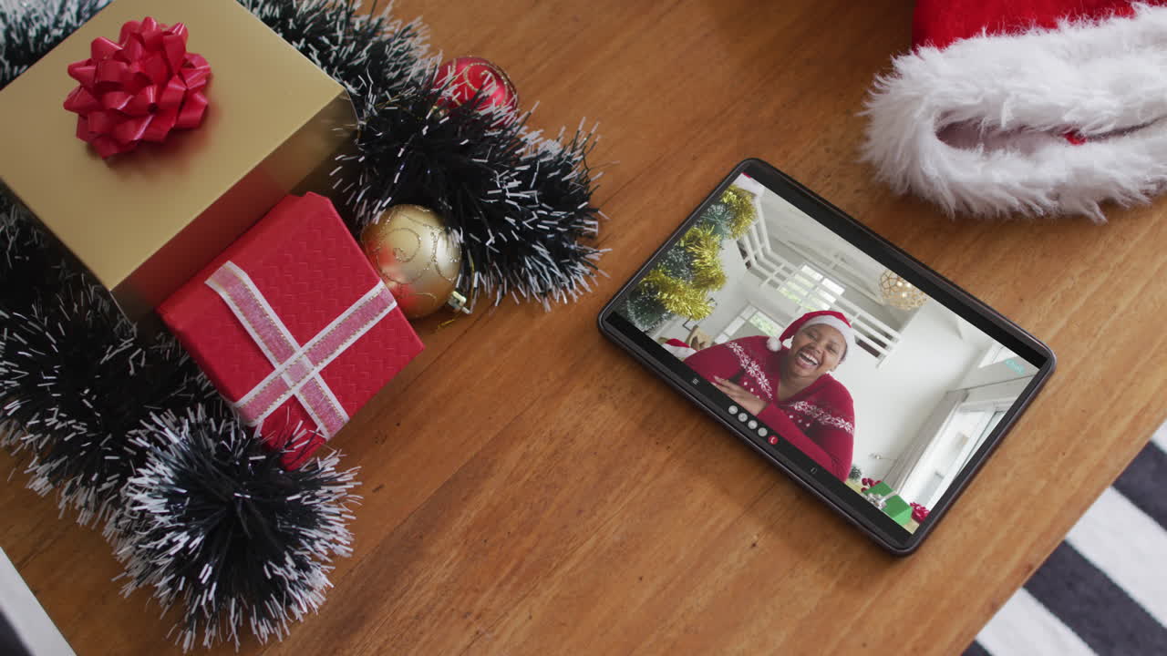 mujer afroamericana sonriente con sombrero de santa en una videollamada de navidad en una tableta