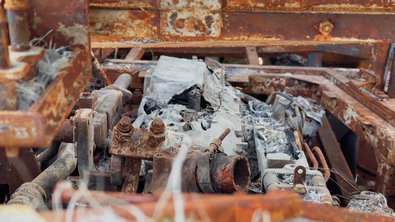 Kamerafahrt von beschädigten Motorkomponenten in einem durch Feuer zerstörten Schlafbus, die verrostete mechanische Teile, geschmolzene Materialien und ein aschebedecktes Metallgerüst zeigt!
