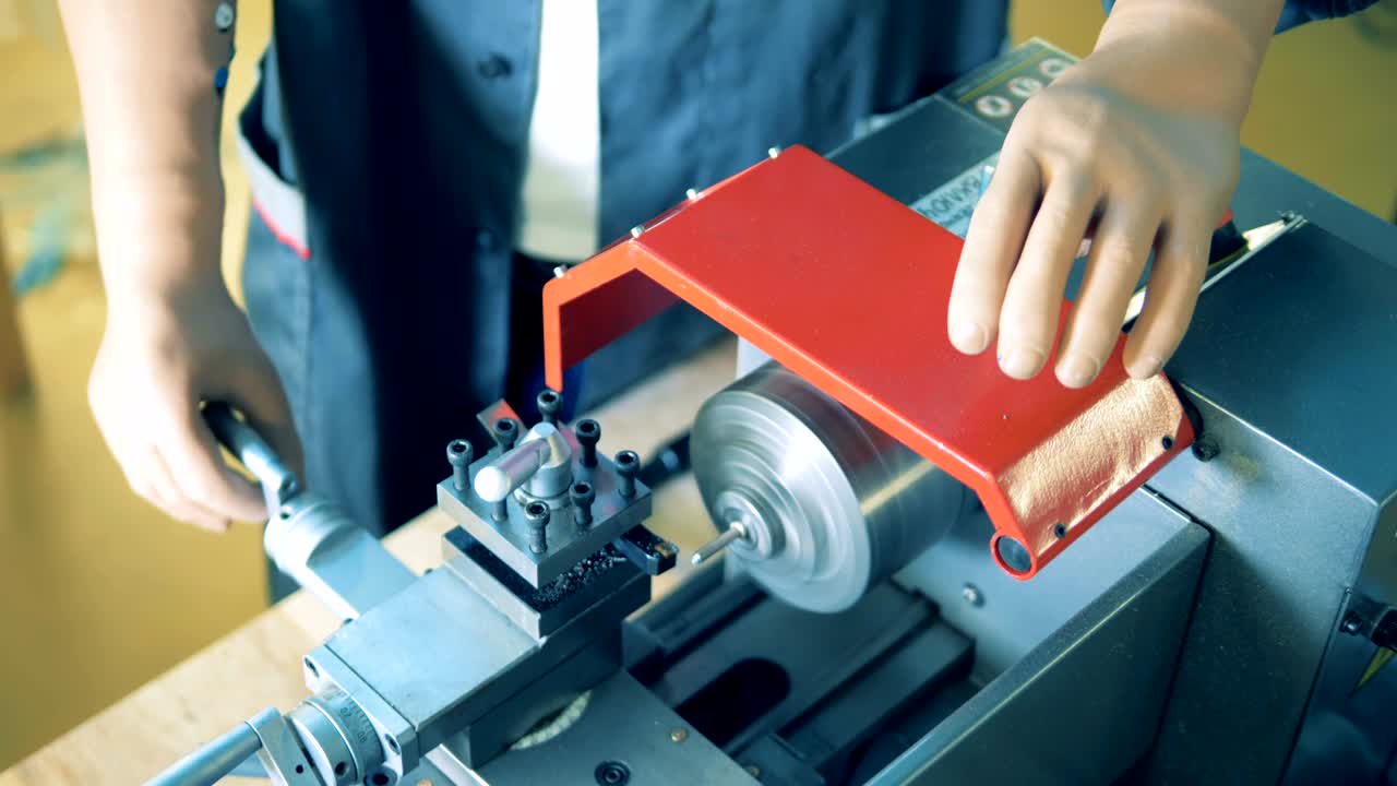 Male worker with prosthetic hands is rotating a handle of a metal lathe