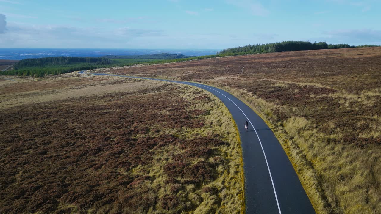 Filmisk droneoptagelse af en cyklist, der cykler gennem Irlands store, lyngdækkede højland. Billedet understreger ensomheden og omfanget af det barske landskab i Dublin Mountains.