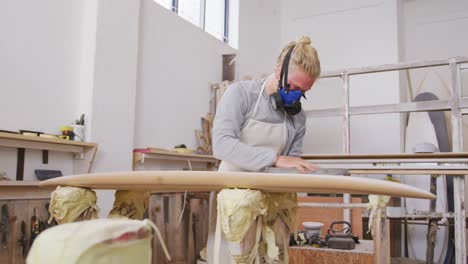 caucasian male surfboard maker wearing a face mask and polishing a surfboard