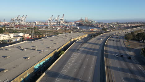 aerial view of a busy freeway leading towards a large shipping port with cranes