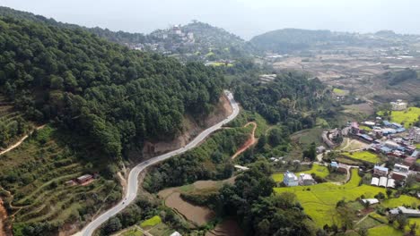 a beautiful aerial view of the himalayan foothills with a road winding along the base of a hill with scattered fields and houses