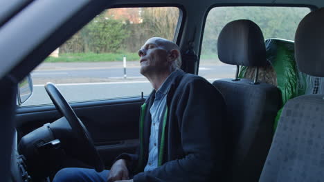 a mature man sleeping in his car at the side of a busy road