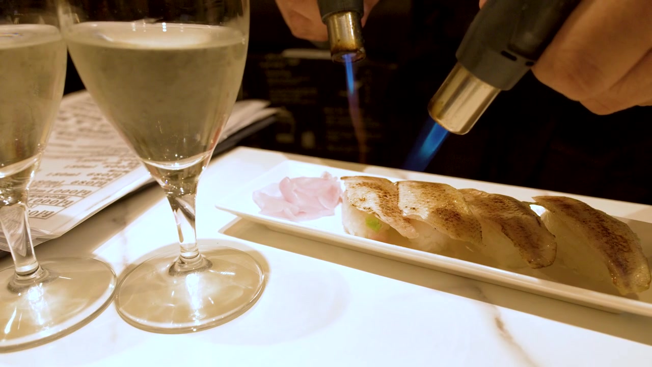 Primo piano di uno chef che scotta nigiri sushi fresco con una torcia a fiamma blu.