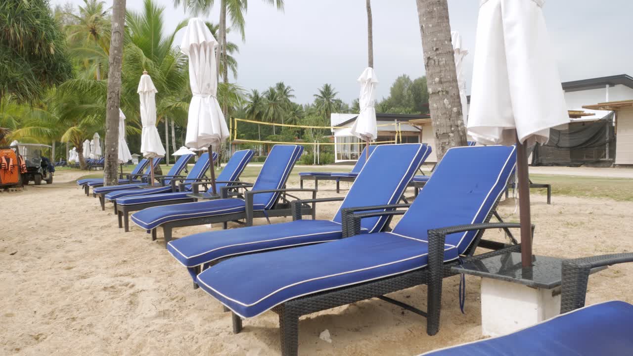 Luxury beach lounge beds with umbrella on white sand beach with coconut tree in thailand with sunny summer weather and clear blue sky