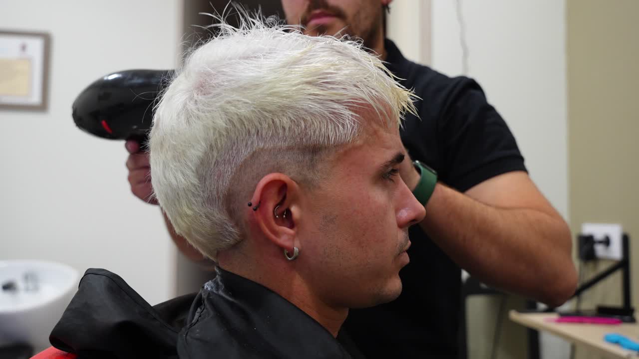 Close profile shot of man receiving hair dryer air as freshly bleached hair is dried and styled