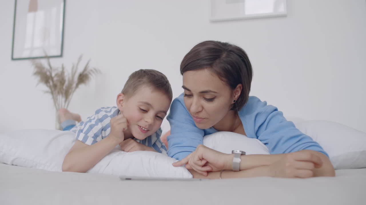 madre joven feliz mostrando dibujos animados en una tableta digital a su hijo pequeño antes de irse a dormir. madre feliz mostrando caricaturas en una tablet digital a su niño pequeño