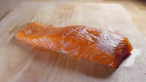 Close-Slow-Motion-Shot-of-Seasoning-a-Fresh-Piece-of-Salmon-Fillet-With-Black-Pepper-Prior-to-Cooking-in-the-Kitchen