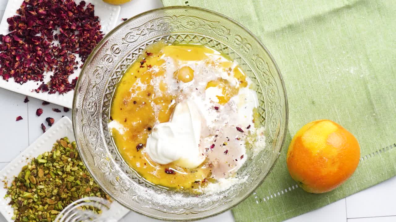 Baking a dessert called Persian Love Cake made with rose petals and pistachios. Cake with white glaze frosting. Using a whisk to combine ingredients. Beautiful cake for tea time or celebration