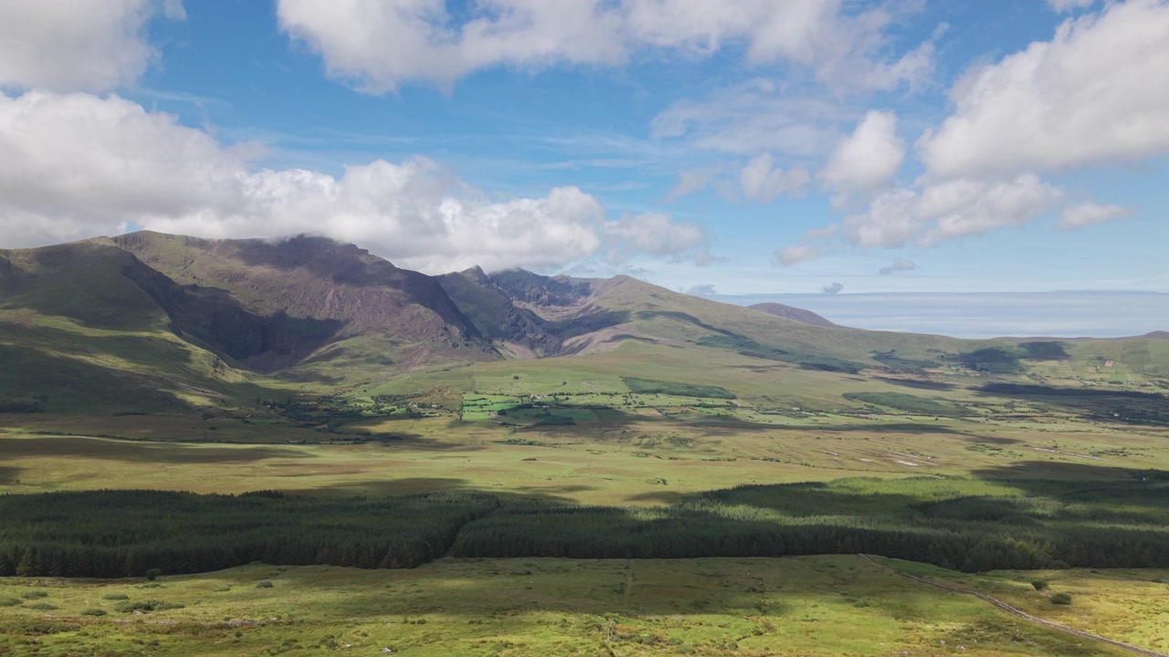 Un'ampia ripresa aerea che cattura le aspre cime del Conor Pass e la lussureggiante valle verde sottostante. Adatto per documentari di viaggio e contenuti sulla sostenibilità ambientale.