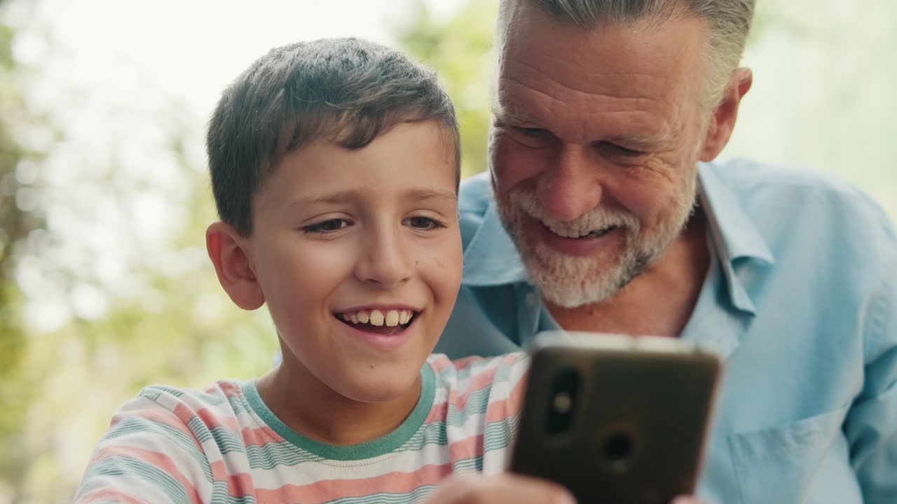 Lille dreng og bedstefar smiler, mens de kigger på smartphone