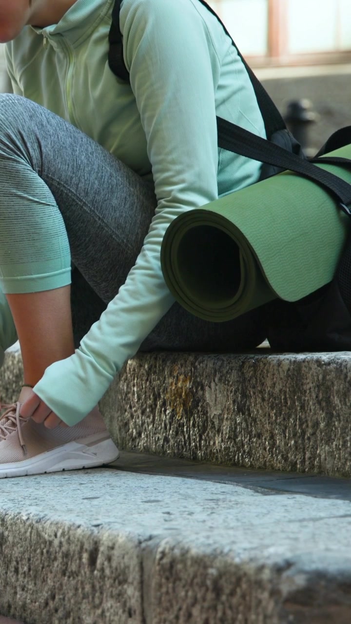 Vertical video: Loose laces making woman tying laces on stone step mint top mat on pack, copy space