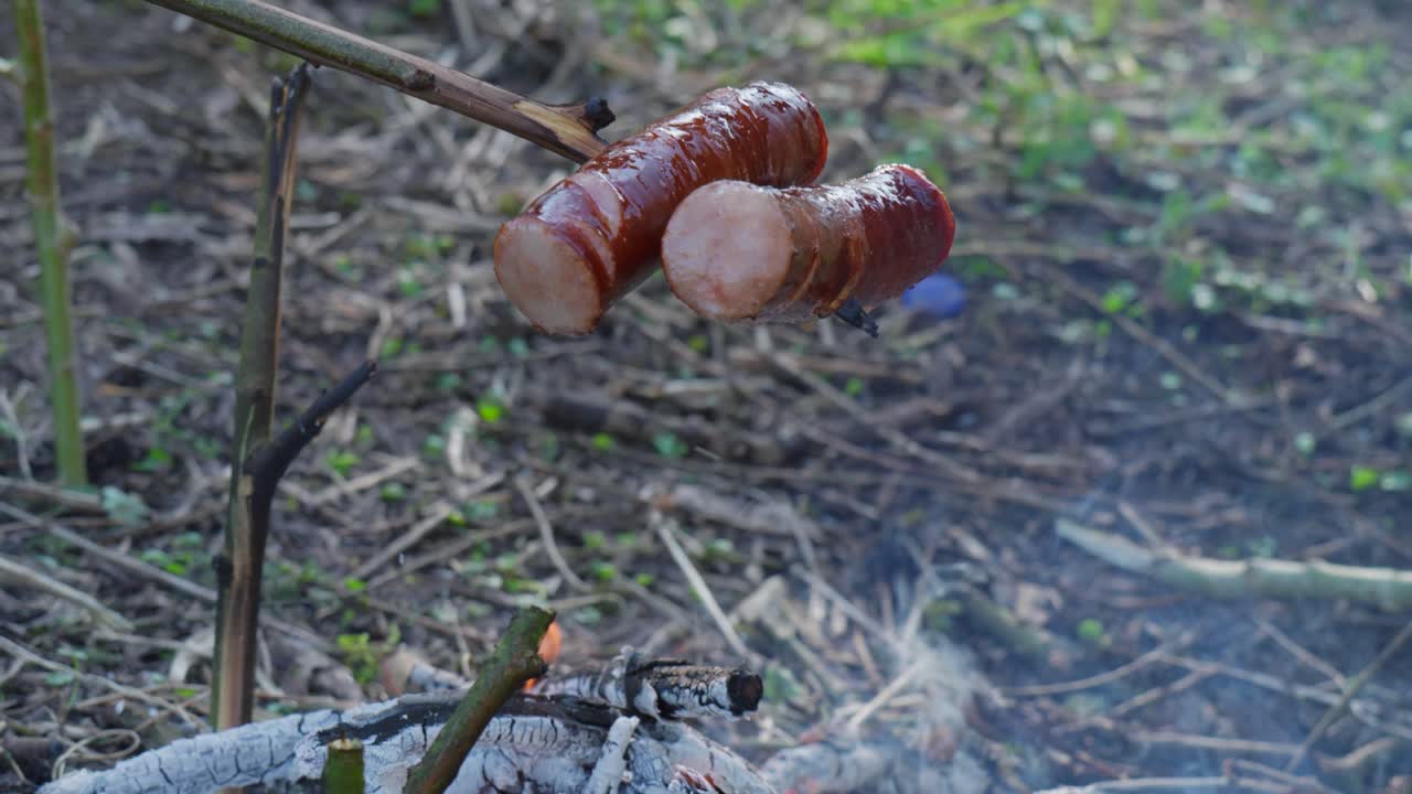 Grilling sausages over an open fire with a rustic outdoor setting