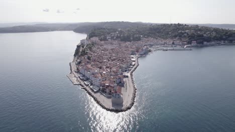 Video-Con-Vista-De-Pájaro-Del-Faro-De-La-Ciudad-De-Piran-En-Eslovenia,-Con-Gente-Caminando-Y-La-Iglesia-De-Fondo