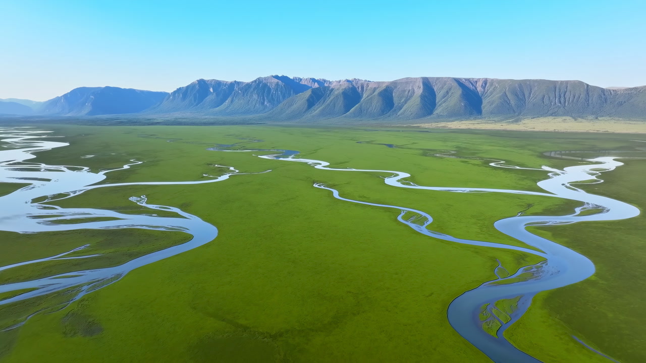 Aerial Winding River Through Emerald Plains Under Clear Blue Sky, Meandering Channels Through Marsh