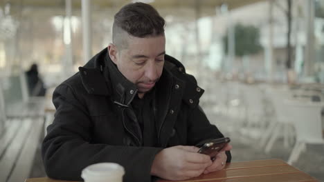 focused man in black coat using smartphone in cafe