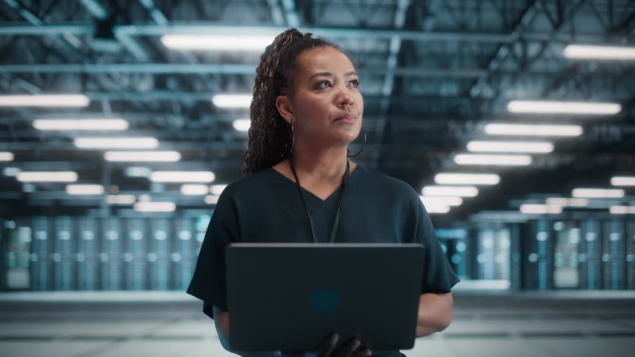 Concept Dolly Zoom Out: Portrait of Black Female Specialist Using Laptop in Big Data Center. Cinematic Shot with High-Tech Special Effect for Technology Science Breakethrough, Progress, Innovation